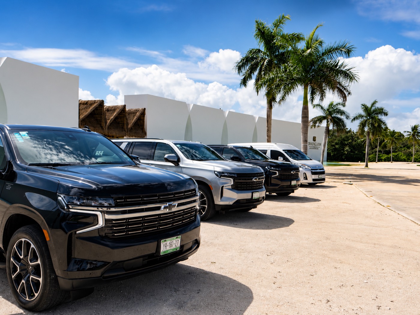 Suburbans y una van de Blue Dreams DMC alineadas junto a palmeras